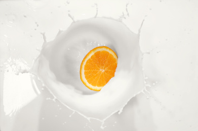 Photo of Slice of orange falling in milk with splash, top view