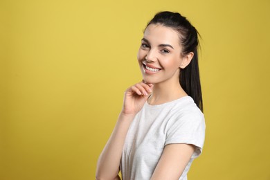Portrait of happy young woman with beautiful black hair and charming smile on yellow background, space for text