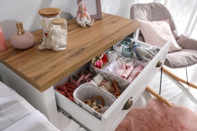 Modern open chest of drawers with baby clothes and accessories in room, closeup