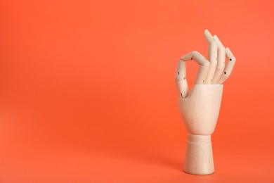 Photo of Wooden mannequin hand showing okay gesture on orange background. Space for text