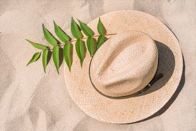 Straw hat and green leaves on sandy beach, top view