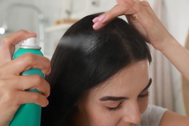 Woman applying dry shampoo onto her hair indoors, closeup