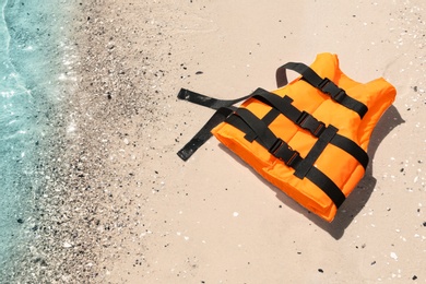 Orange life jacket on sand near sea, above view. Emergency rescue equipment
