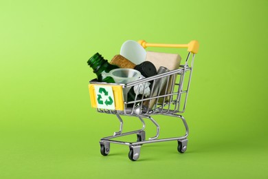 Photo of Shopping cart with recycling symbol full of garbage on light green background