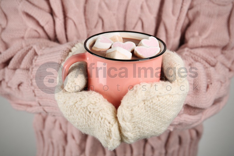 Woman in knitted mittens holding cup of delicious hot chocolate with marshmallows, closeup