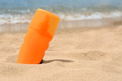 Photo of Bottle with sun protection spray on sandy beach near sea, closeup. Space for text