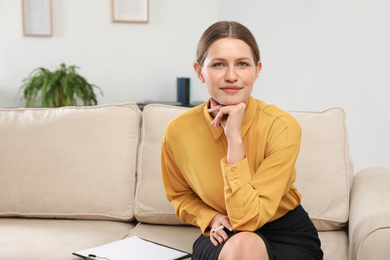 Professional psychotherapist with clipboard on sofa in office