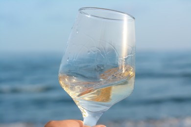 Photo of Glass of tasty wine near sea, closeup