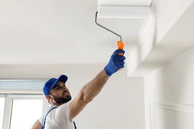 Handyman painting ceiling with white dye indoors, focus on roller