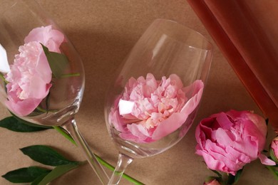 Bottle of rose wine, glasses and beautiful pink peonies on brown background, closeup