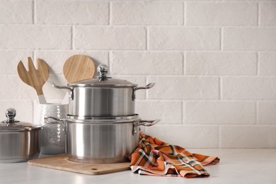 Set of stainless steel cookware and kitchen utensils on table near white brick wall, space for text