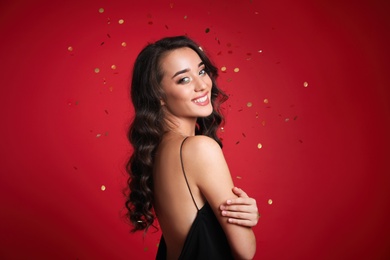 Beautiful young woman wearing elegant dress on red background. Christmas party