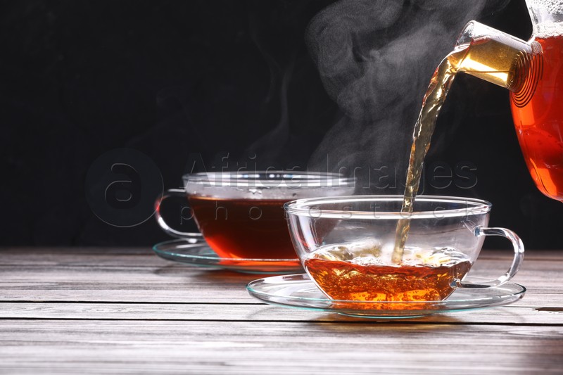 Photo of Pouring tea into glass cup on wooden table against black background, space for text