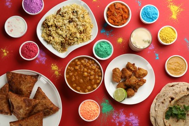 Traditional Indian food and color powder dyes on red background, flat lay. Holi festival