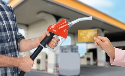 Woman holding credit card and worker with fuel nozzle at gas station, closeup. Cashless payment