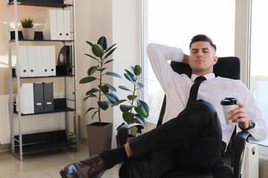 Photo of Businessman with hot drink relaxing in office chair at workplace