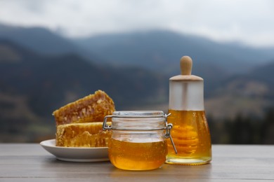 Fresh aromatic honey and combs on grey wooden table against mountain landscape