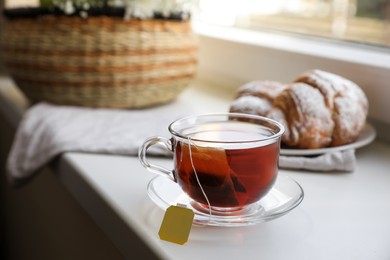Photo of Tea bag in glass cup on white windowsill. Space for text