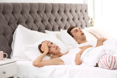 Young irritated woman lying on pillows in bed at home. Problem with snoring husband