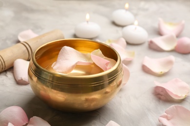 Golden singing bowl with petals and mallet on grey table, closeup. Sound healing