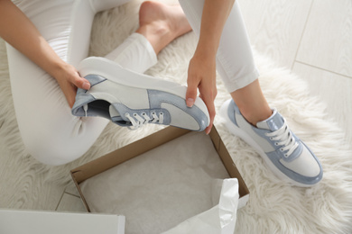 Woman measuring new stylish sneakers indoors, closeup