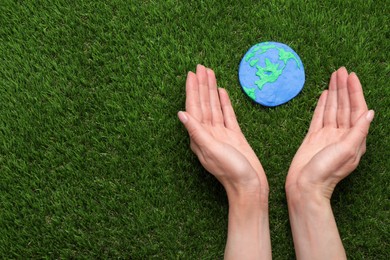 Happy Earth Day. Woman with plasticine planet on green grass, top view and space for text