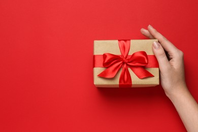 Woman holding beautiful gift box on red background, top view. Space for text