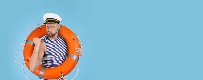 Sailor with orange ring buoy showing his strength on light blue background