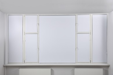 Large window with closed white roller blinds indoors