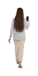 Photo of Young woman in casual outfit using smartphone while walking on white background, back view