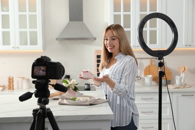 Blogger with tasty cake recording video in kitchen at home. Using ring lamp and camera