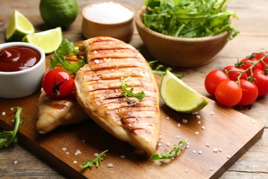 Tasty grilled chicken fillets with tomato and lime on wooden board, closeup