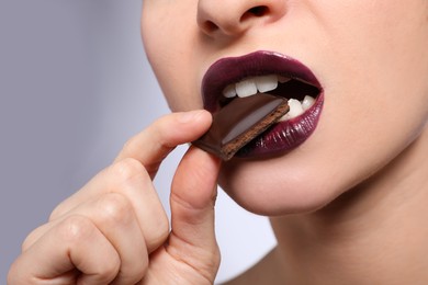 Young woman with beautiful lips makeup eating chocolate on light background, closeup