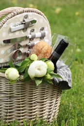 Photo of Picnic basket with wine, bread and flowers on green grass outdoors