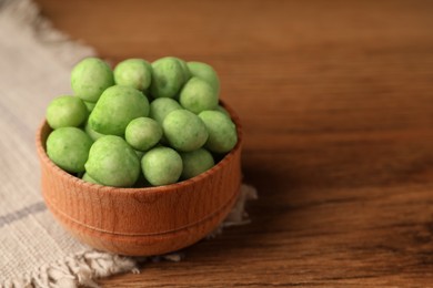 Tasty wasabi coated peanuts in bowl on brown wooden table, closeup. Space for text