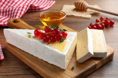 Photo of Brie cheese served with red currants and honey on wooden table, closeup