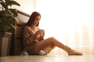 Woman with cup of drink sitting on warm floor at home. Heating system