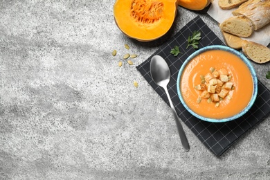 Tasty creamy pumpkin soup served with bread on grey table, flat lay. Space for text