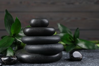 Photo of Stacked spa stones and bamboo leaves on black textured table, closeup