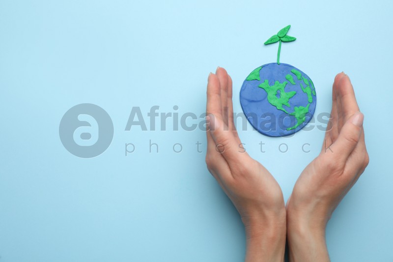 Woman near plasticine model of planet with green seedling and space for text on light blue background, top view. Earth Day