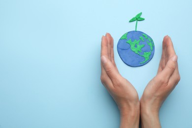 Woman near plasticine model of planet with green seedling and space for text on light blue background, top view. Earth Day