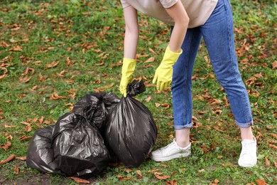 Woman holding plastic bags with garbage in park, closeup.