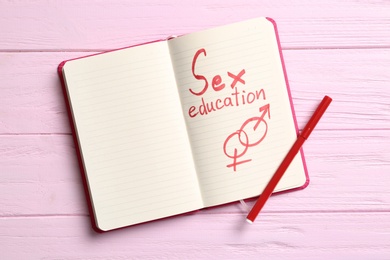 Notebook with phrase "SEX EDUCATION" and gender symbols on pink wooden background, top view. Space for text