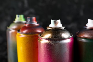 Photo of Used cans of spray paint on black marble background, closeup