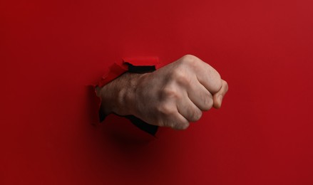 Man breaking through red paper with fist, closeup