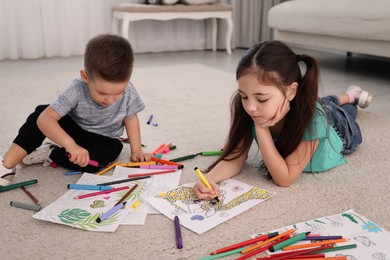Cute children coloring drawings on floor at home