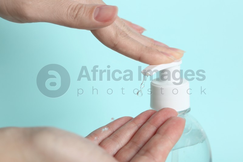 Woman applying antiseptic gel on hand against light blue background, closeup
