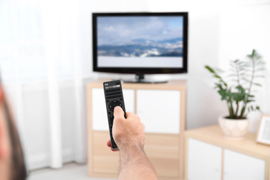 Image of Man switching channels on modern TV set with remote control at home