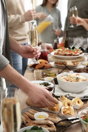 Photo of Man with glass of champagne taking food from buffet indoors, closeup. Brunch table setting