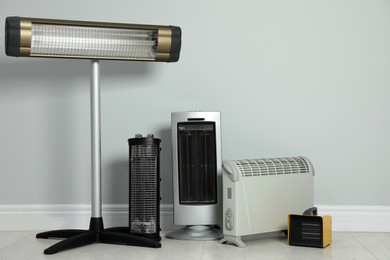 Different electric heaters near light grey wall indoors. Space for text